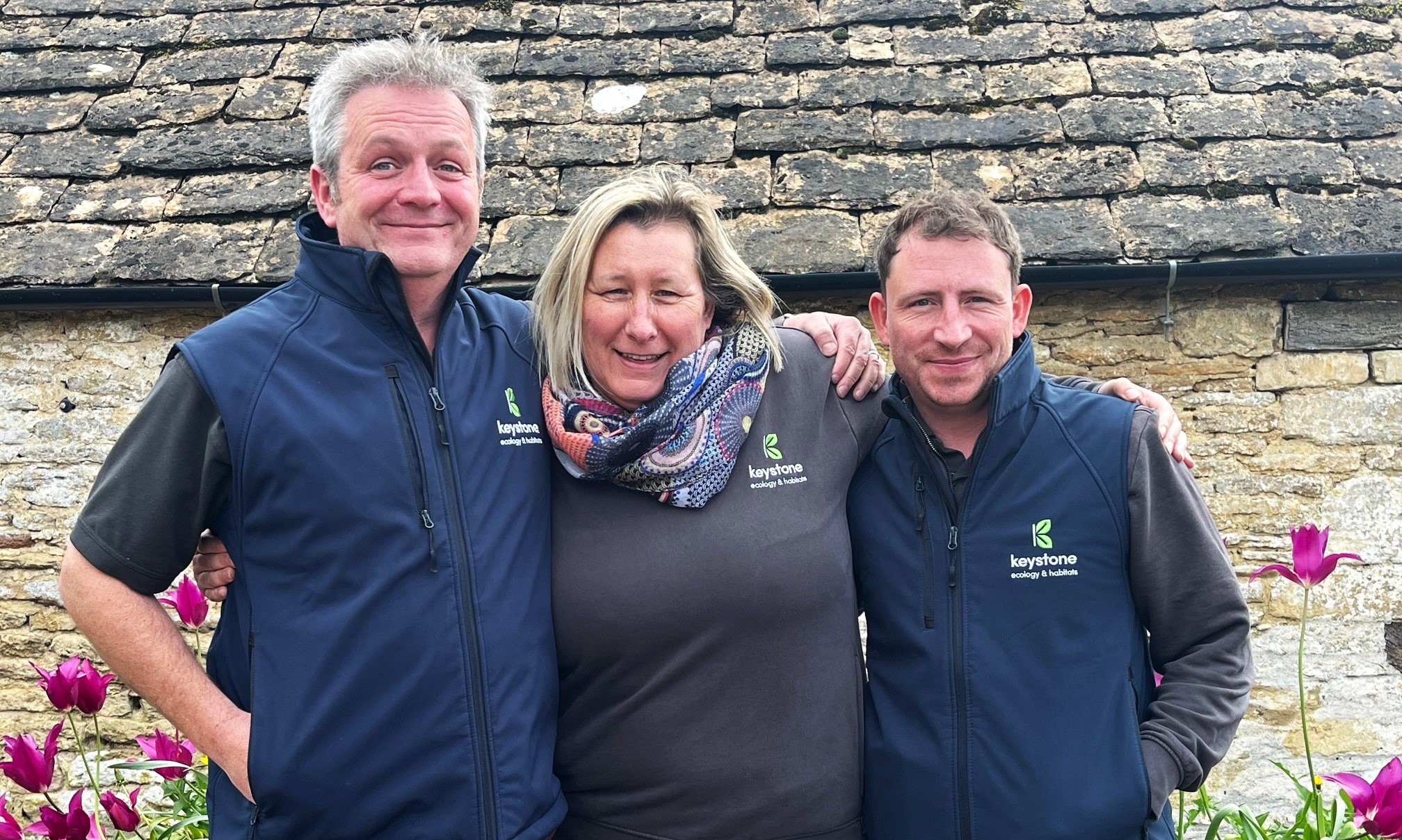 Team hugging for a photo in front of an old stone cottage